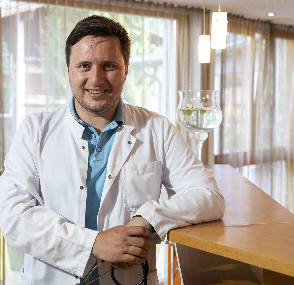 Medizin trifft Erholung – Dr Martin Ortner im Naturhotel Eschenhof in Bad Kleinkirchheim Dr Martin Ortner Allgemeinmediziner und Wahlarzt im weißen Kittel an der Rezeption seiner Praxis im Naturhotel Eschenhof in Bad Kleinkirchheim